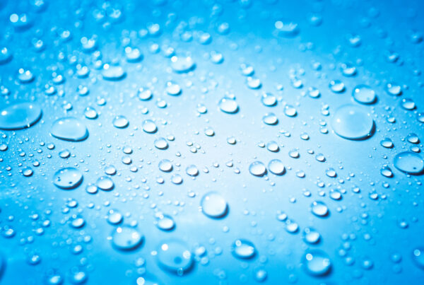 Macro shot of water droplets beading on a smooth, non-porous blue Pond Shield epoxy surface.