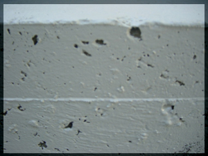 Close-up of large deep pits and voids in a concrete pond surface that require filling before applying Pond Shield epoxy
